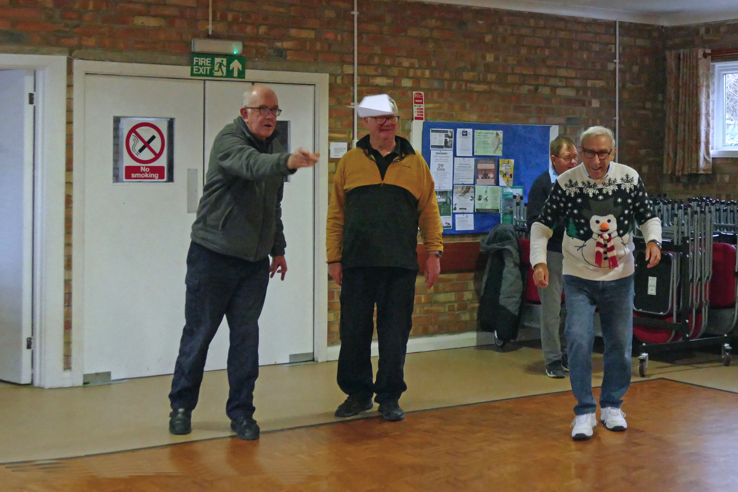 Chris Grant tries to give his paper dart extra height by bouncing it off Andy’s head whilst Bert spots the Christmas food has now arrived for the Christmas party/auction